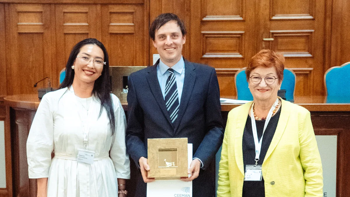 Johannes Siebert hält den CEEMAN Champion Award, flankiert von Aigerim Kaumenova und Danica Purg in einem holzgetäfelten Hörsaal in Bukarest.